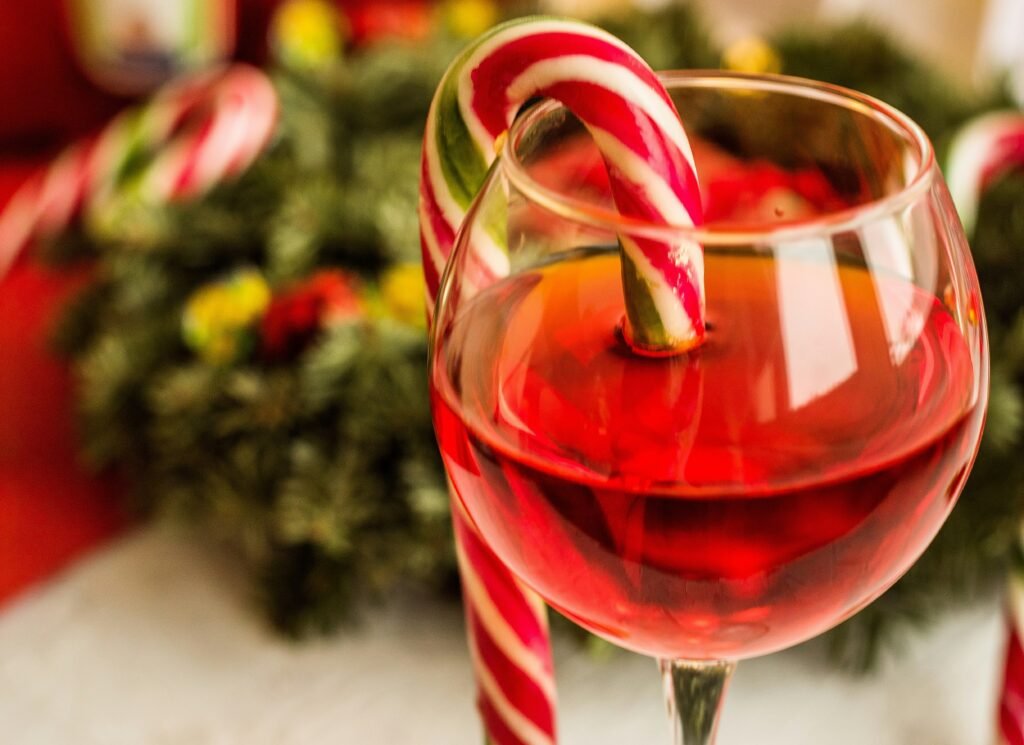 wine glass with red liquid and a candy cane hanging off the edge